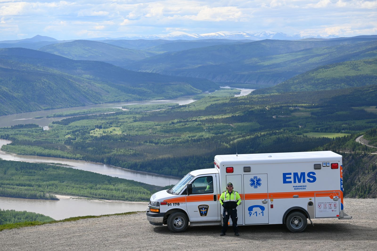 A paramedic is seen in Dawson City standing next to an ambulance on the scenic Dome Road lookout