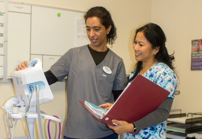 2 people standing by a medical equipment. 