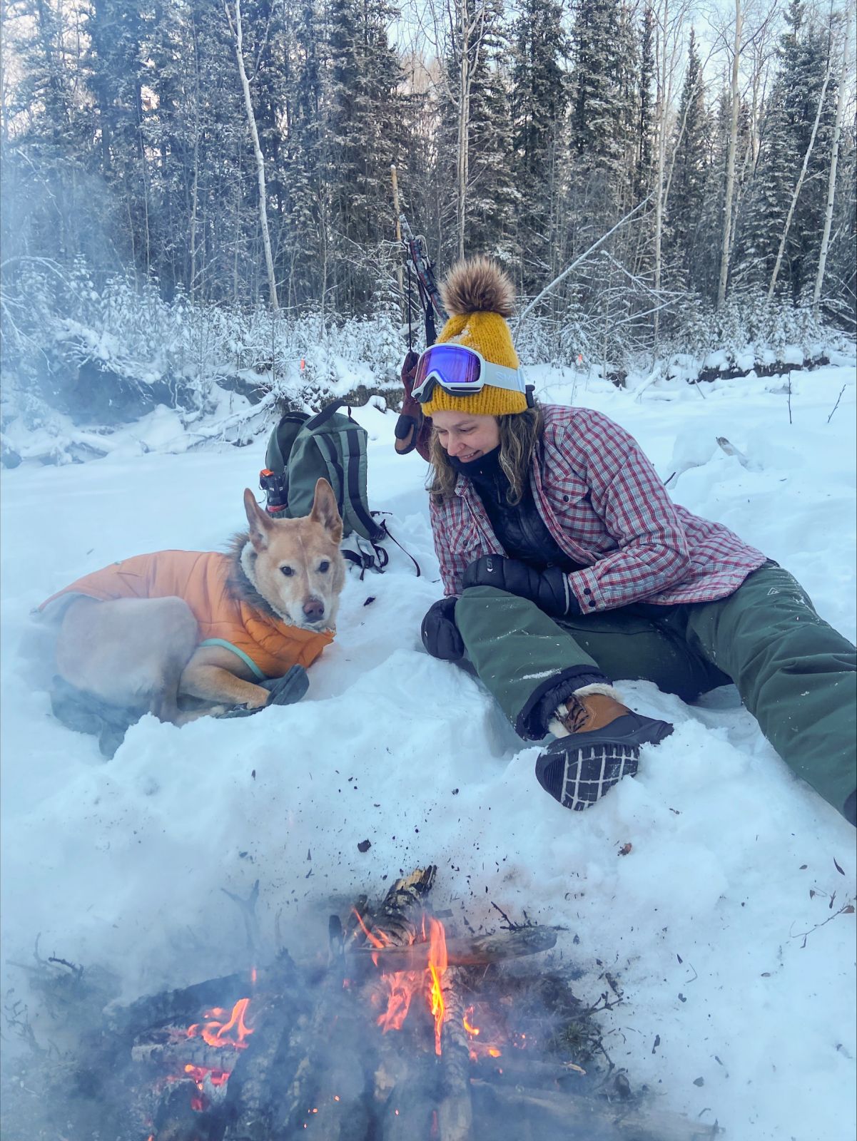 A social worker in the Yukon is seen relaxing alongside a dog near a camp fire