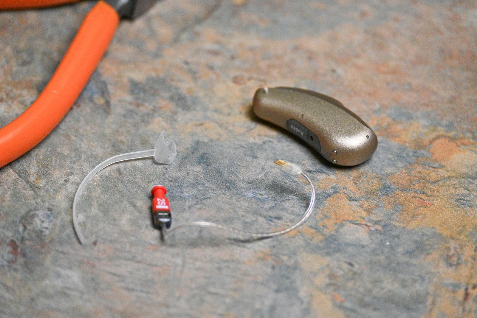 A hearing aid is shown on the repair shop table at Hearing Services