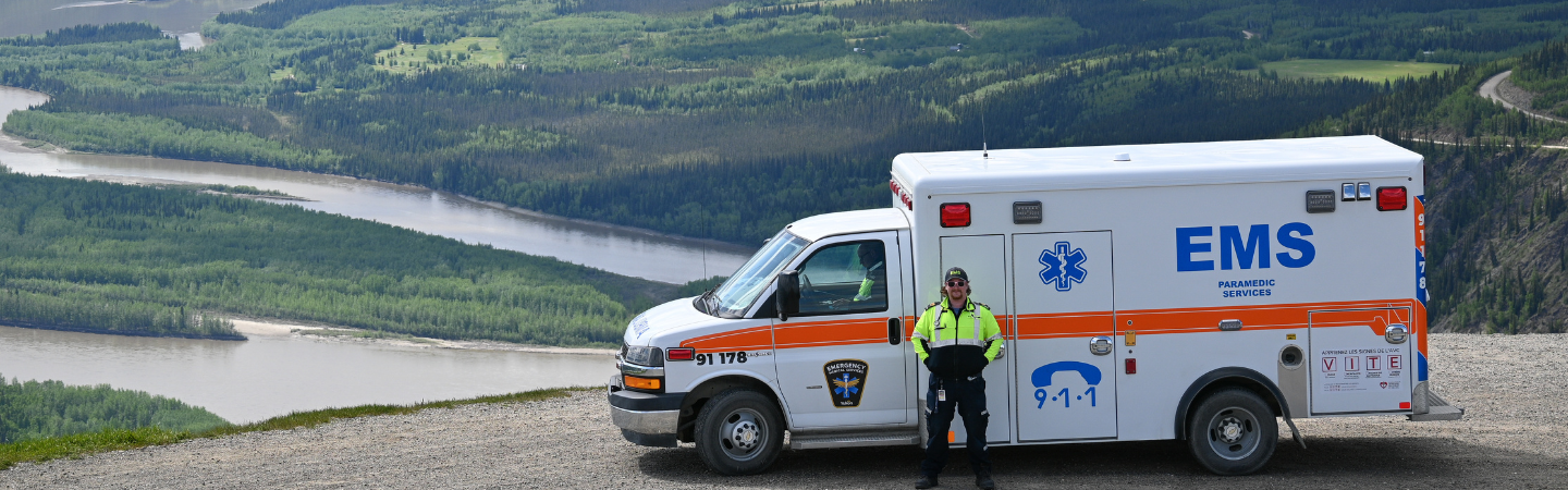 A paramedic is seen in Dawson City standing next to an ambulance on the scenic Dome Road lookout