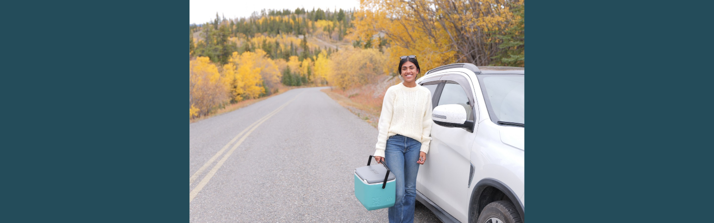 A home care nurse in the Yukon is shown standing alongside her vehicle in fall colours.